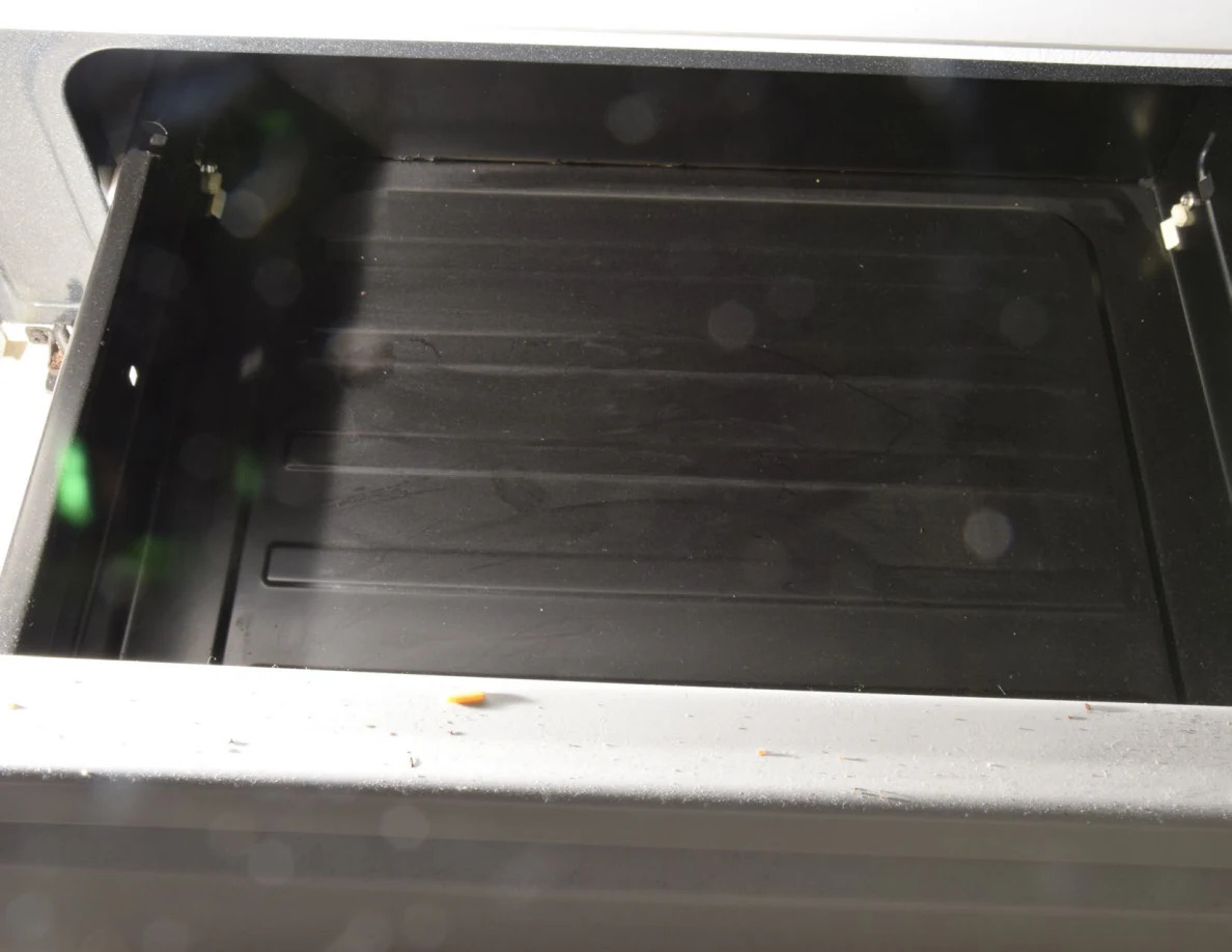 Open oven storage drawer viewed from above, showing a dark ribbed base.