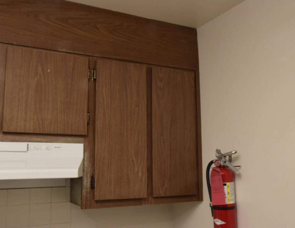 Closed wooden upper kitchen cabinets beside a wall-mounted red fire extinguisher.
