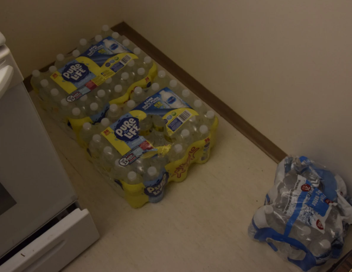Packs of bottled water on the kitchen floor beside a stove.