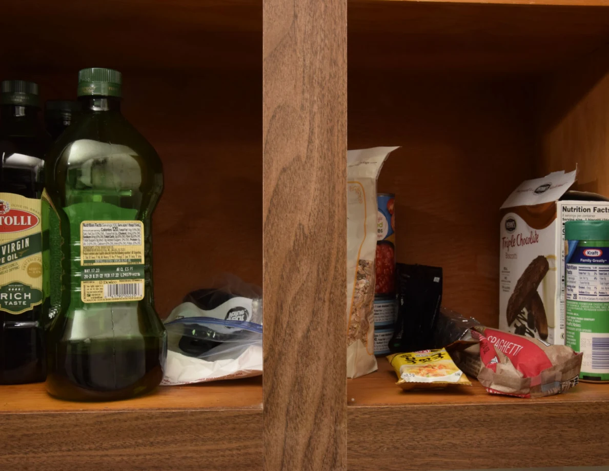 Food cupboard shelf with olive-oil bottles, boxed goods and packets.