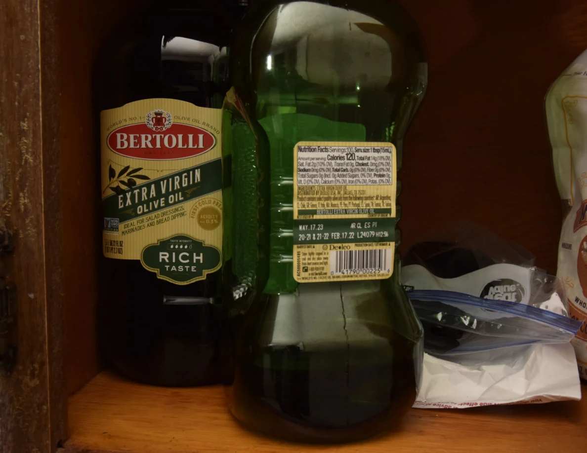 Close view of olive-oil bottles and a plastic bag on a wooden cupboard shelf.