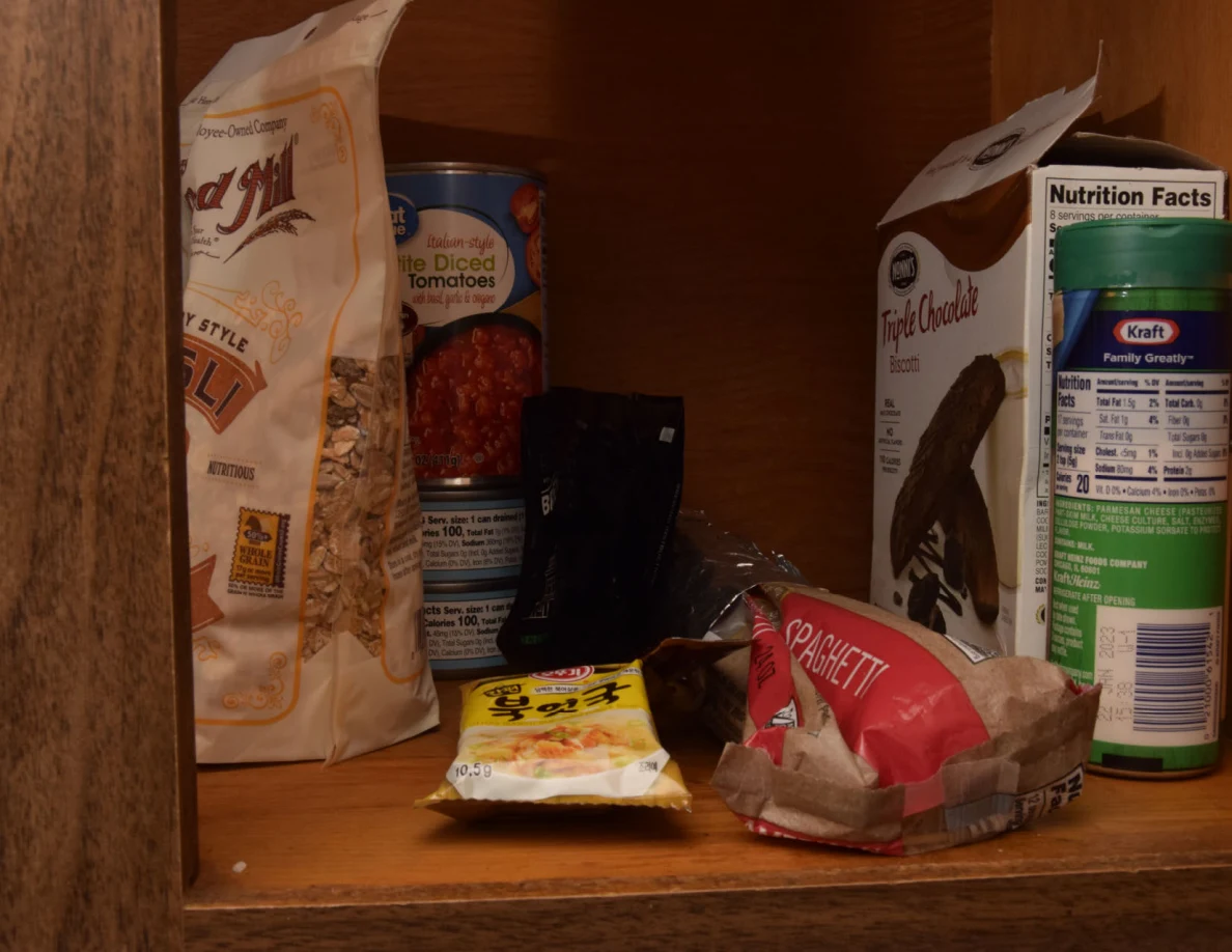 Cupboard shelf with canned tomatoes, dry-food bags, a boxed mix and a grated-cheese container.