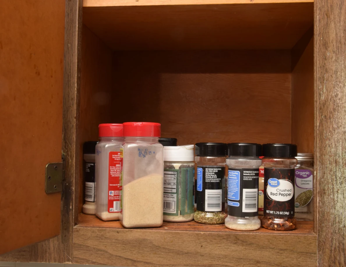 Open cupboard containing rows of spice and seasoning containers.