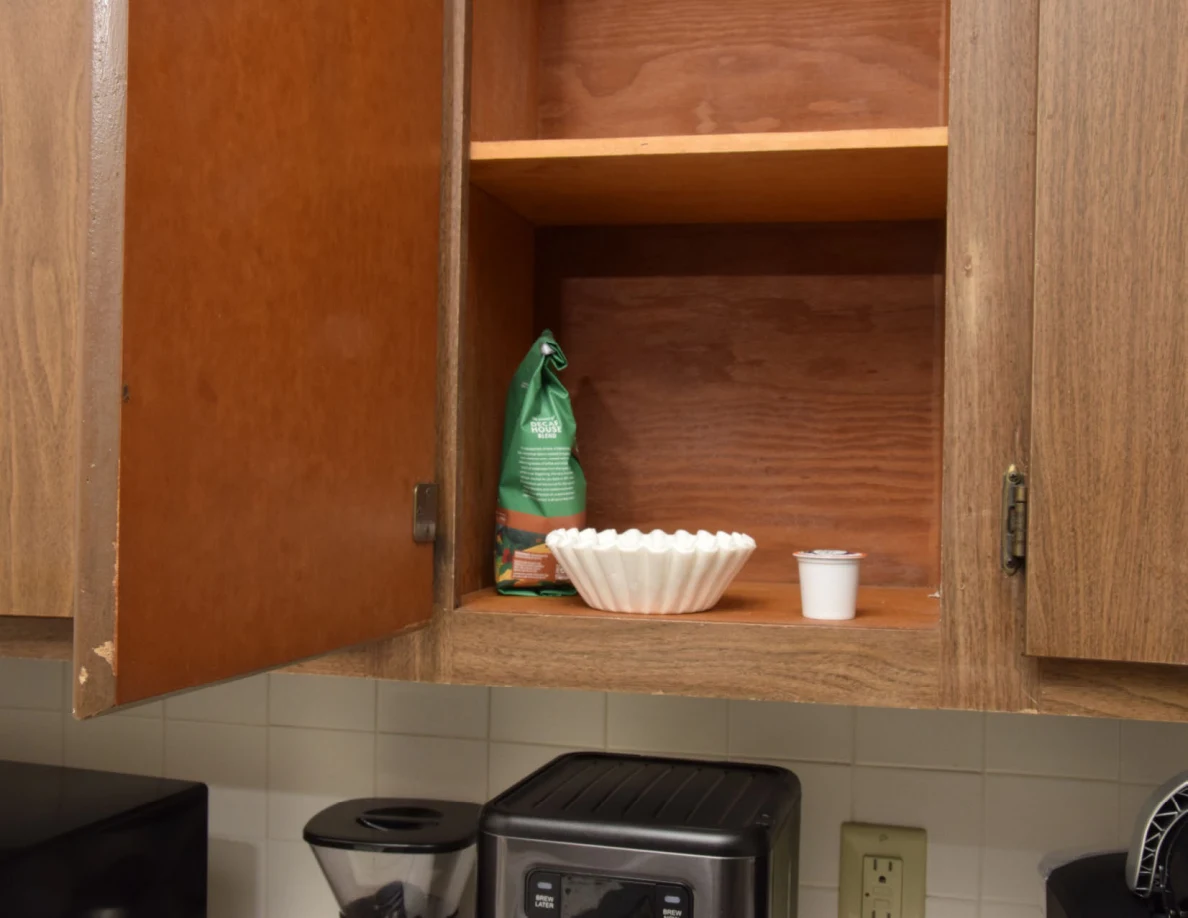 Open cupboard with a coffee bag, stack of paper filters and a single-serve pod above countertop appliances.