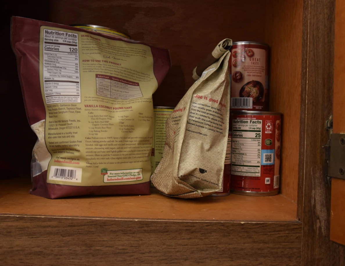 Dry-food bags and stacked cans on a wooden pantry shelf.