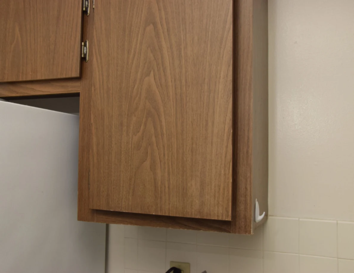 Closed tall wooden kitchen cupboard door beside a refrigerator.