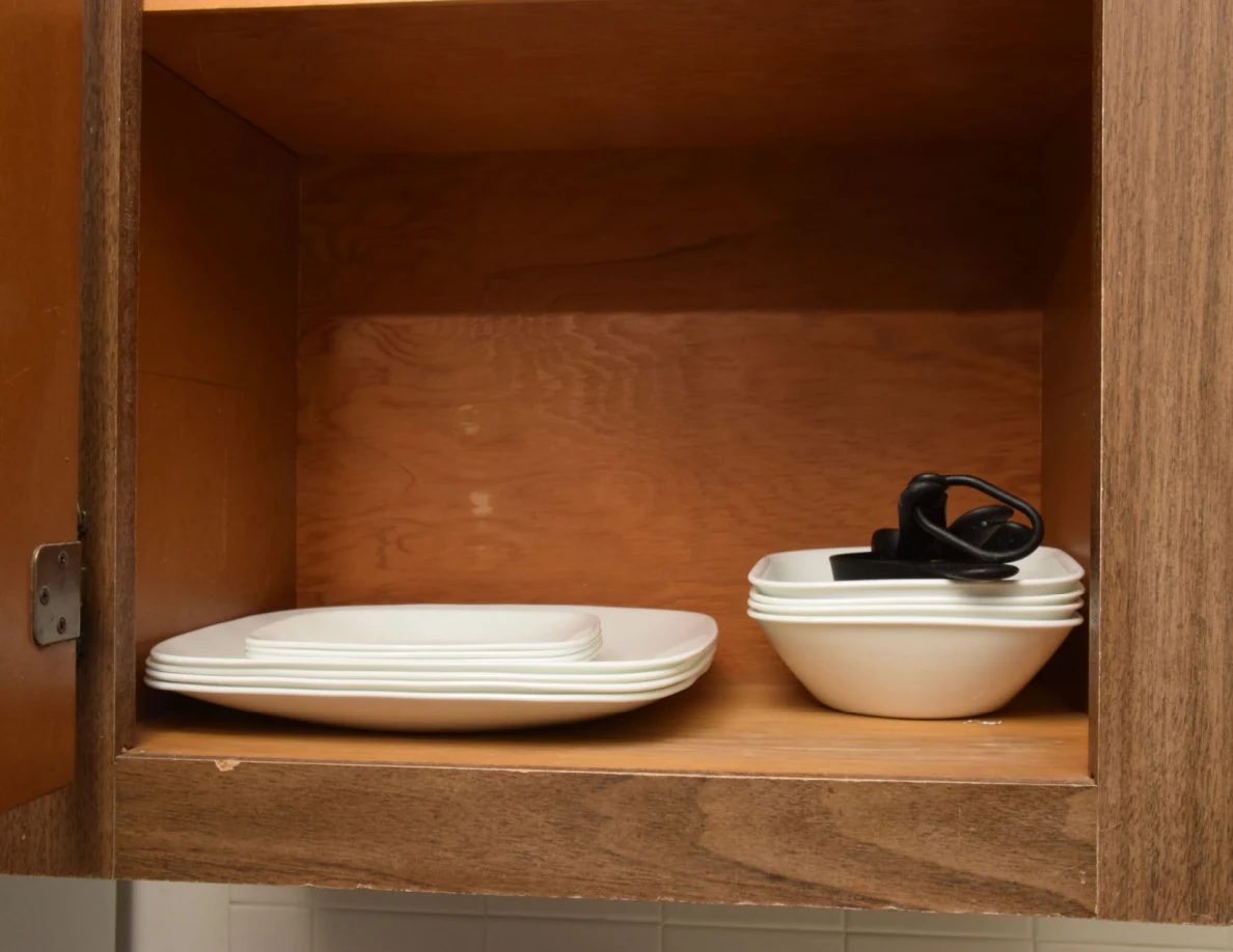 Stacked white plates and bowls with black kitchen utensils in an open cupboard.
