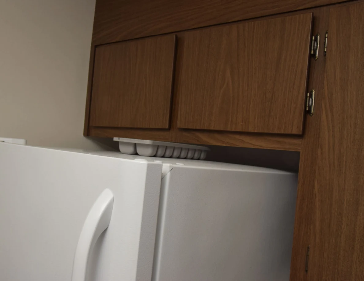Closed wooden cabinet doors above a white refrigerator, with a white tray in the gap below.