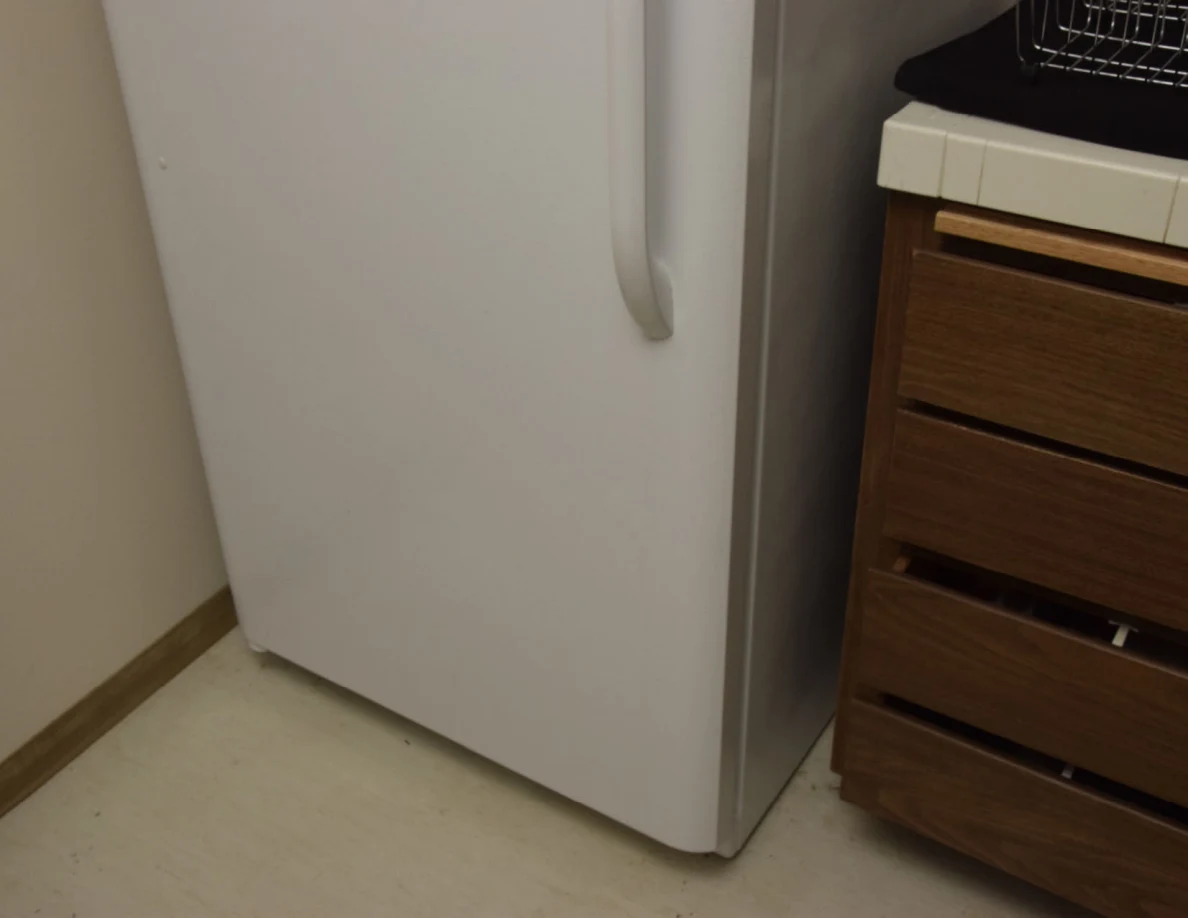 Lower white refrigerator door beside wooden kitchen drawers and a tiled counter.