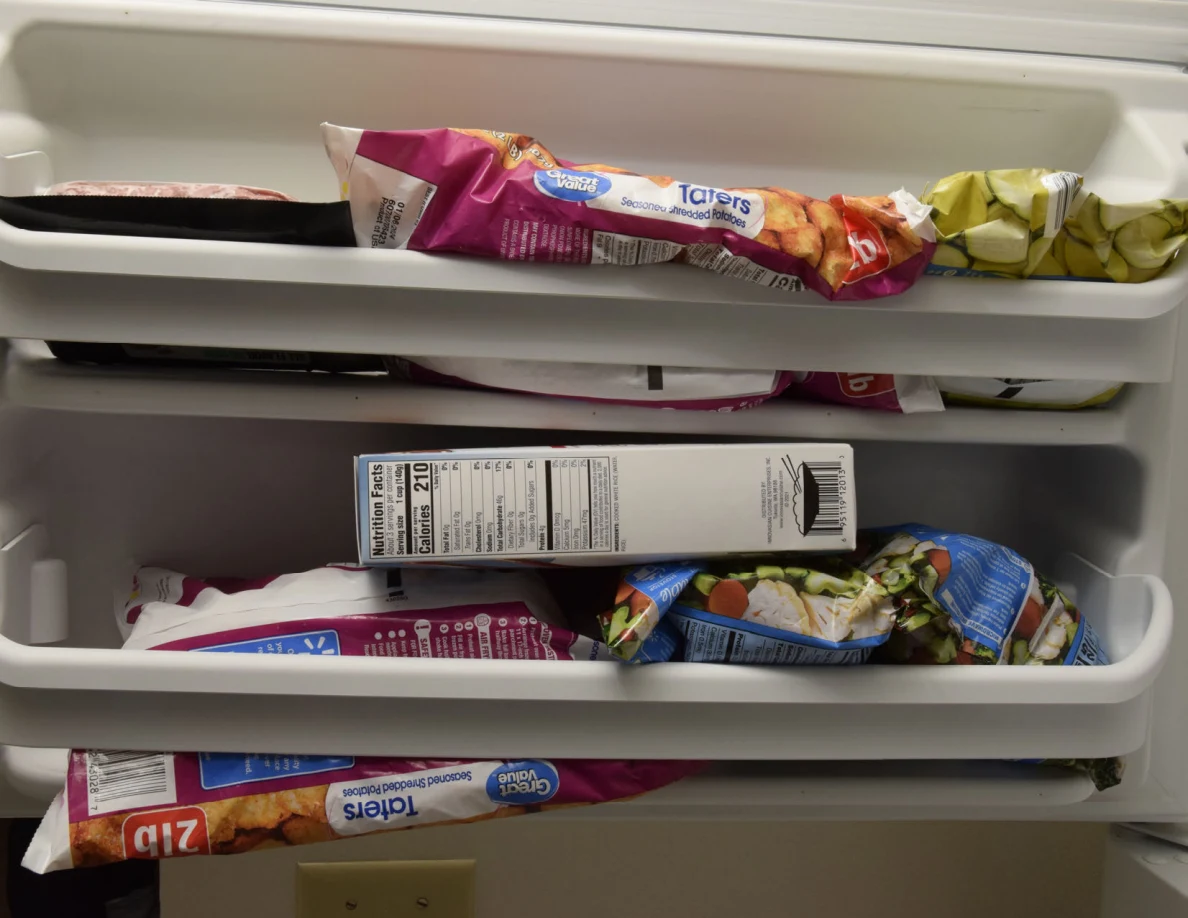 Freezer door shelves holding frozen-food bags, including tater tots, and a boxed item.