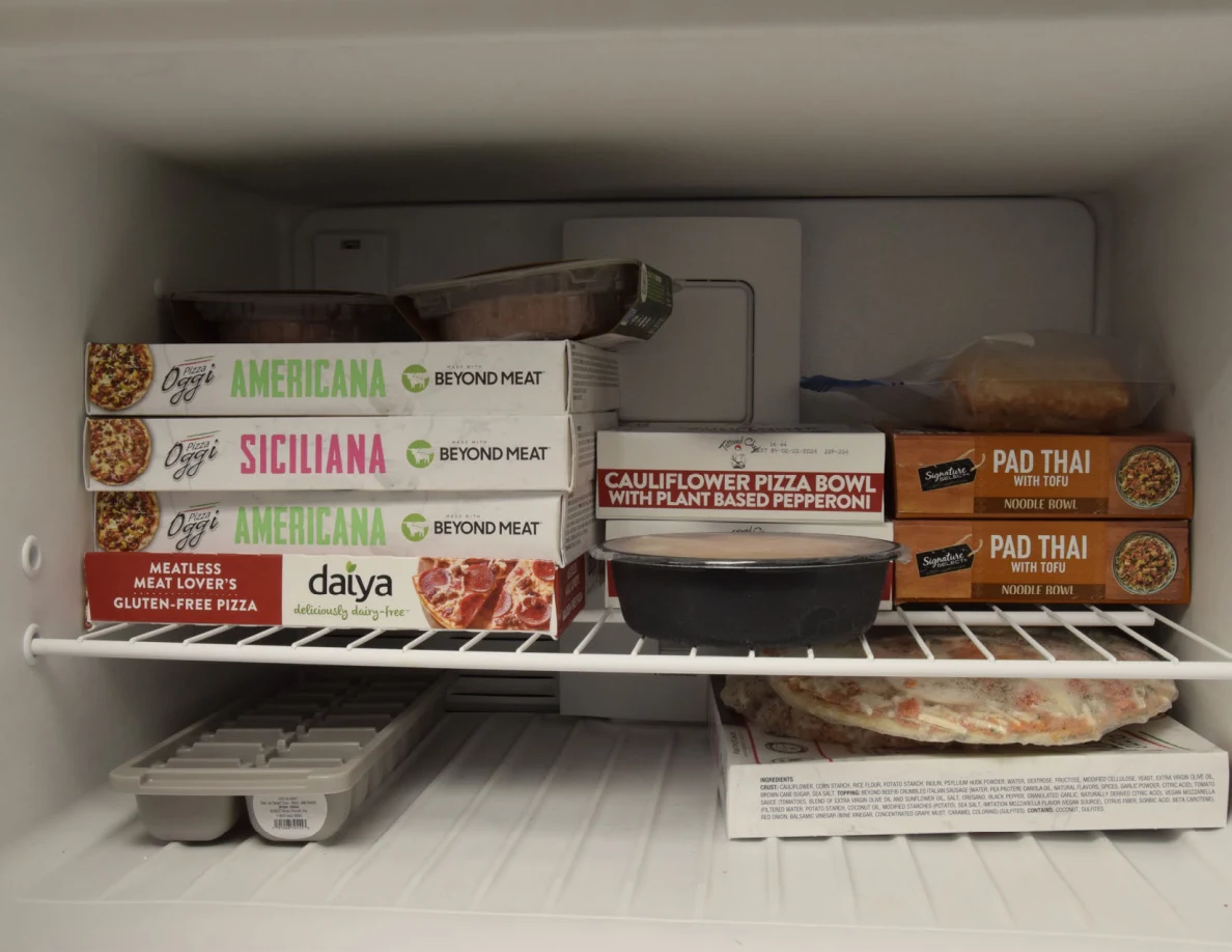 Freezer interior with stacked pizza and prepared-meal boxes, containers and ice trays.