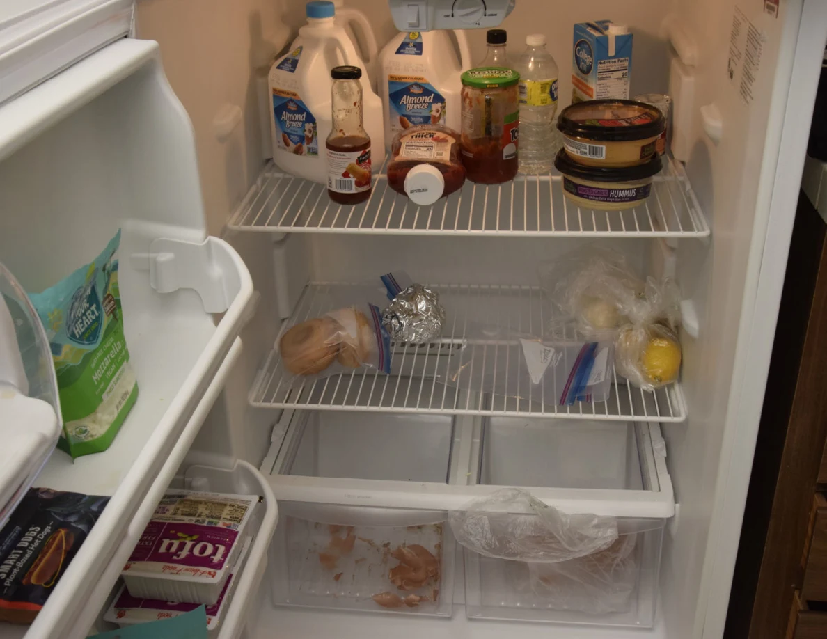 Refrigerator interior with cartons, jars, sauces, wrapped food and mostly empty lower shelves.