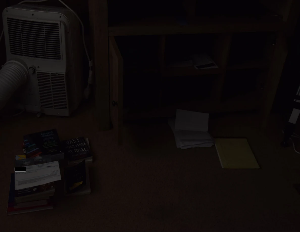 Dim room view with a portable air conditioner, wooden cabinet and books and papers on the carpet.