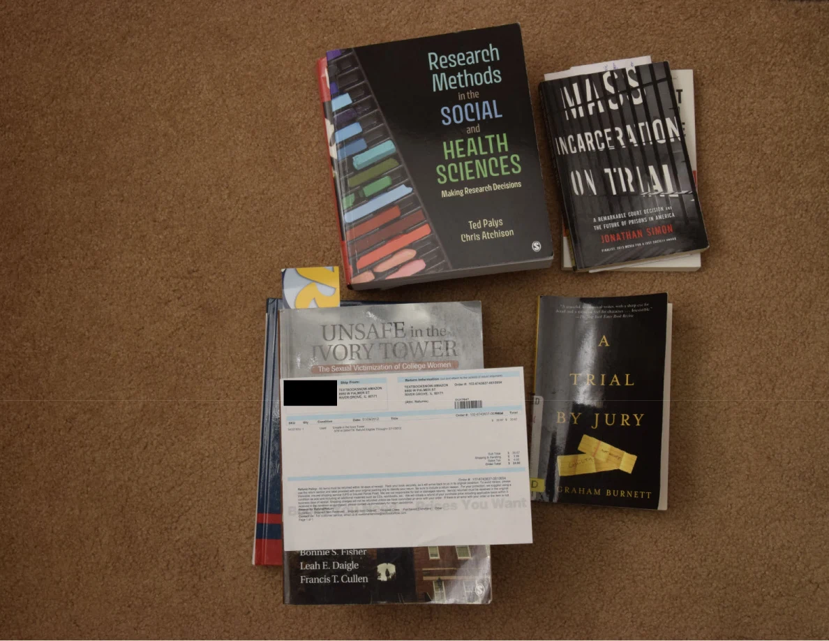 Books about research methods, incarceration and jury trials on a carpet, with a redacted paper across one stack.