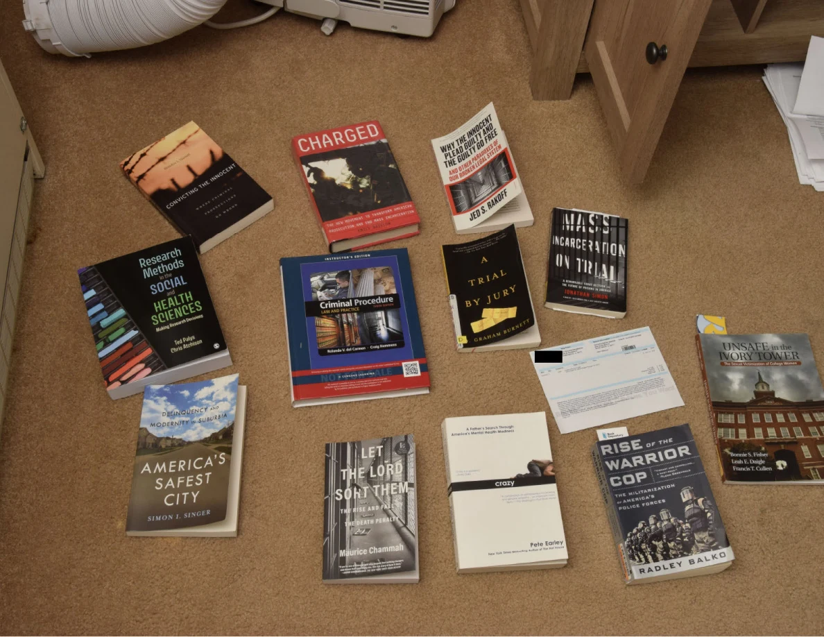 Several books about criminal justice, policing, incarceration and research arranged on a carpet beside an open cabinet.
