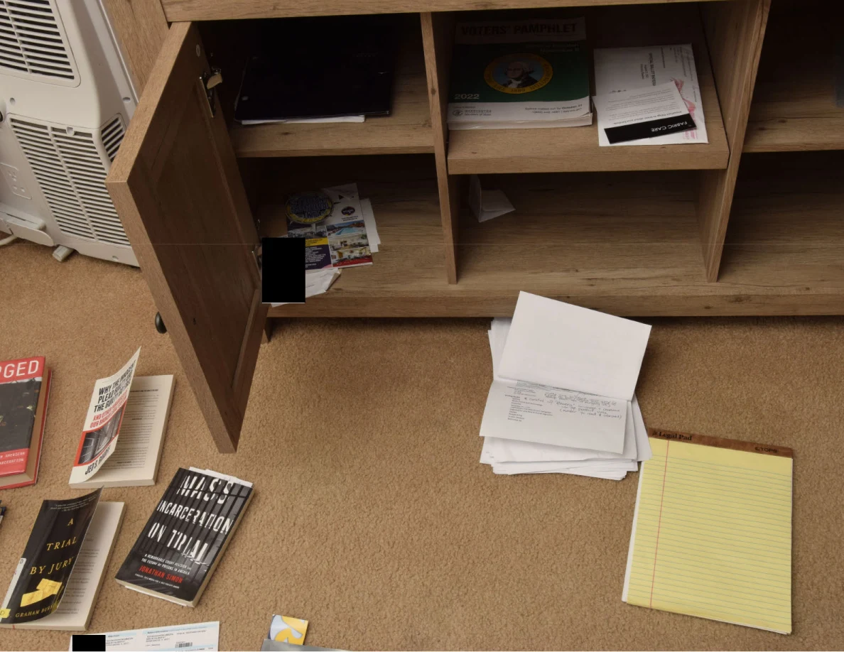 Open wooden cabinet with booklets and papers, with loose papers and a yellow legal pad on the floor.