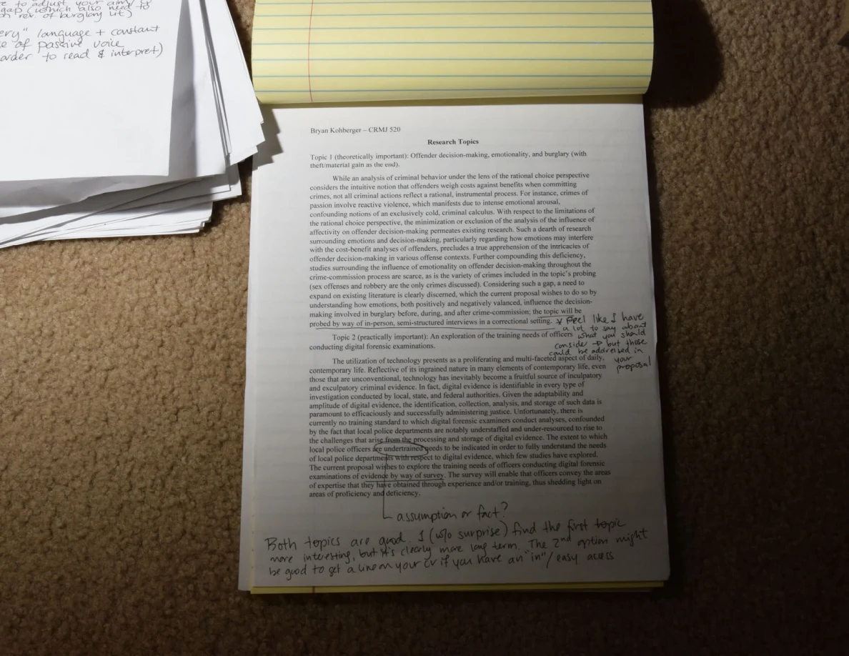 Printed research-topic page with handwritten notes beneath a folded-back yellow legal pad.
