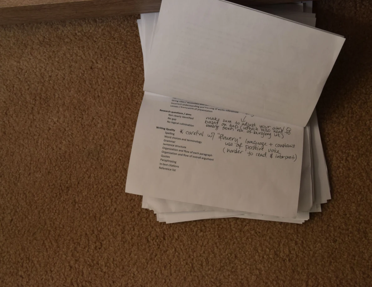 Stack of printed pages on carpet, with a partly folded sheet and handwritten notes on top.