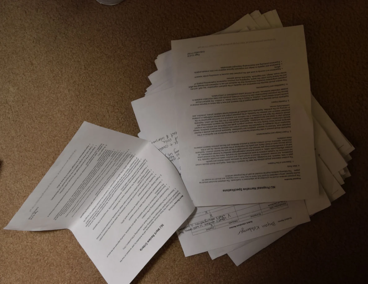 Loose printed pages and handwritten notes spread over a stack on carpet.