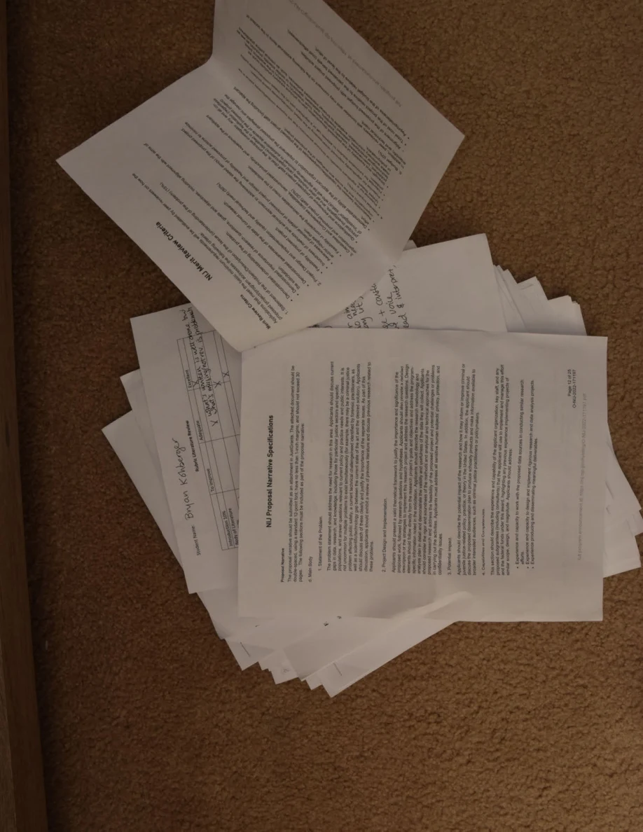 Overlapping printed pages on carpet, including a page lifted diagonally above the stack.