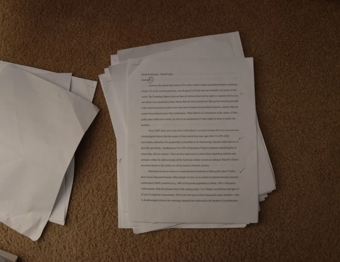 Stack of printed essay pages on carpet, with a small handwritten mark near the top.