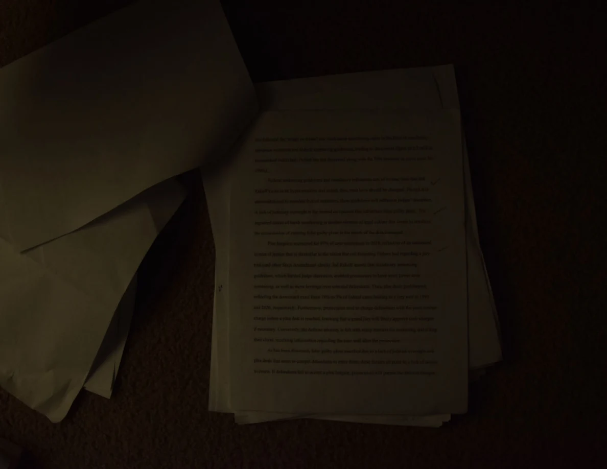 Dim photograph of a printed page beneath a turned sheet, resting on carpet.