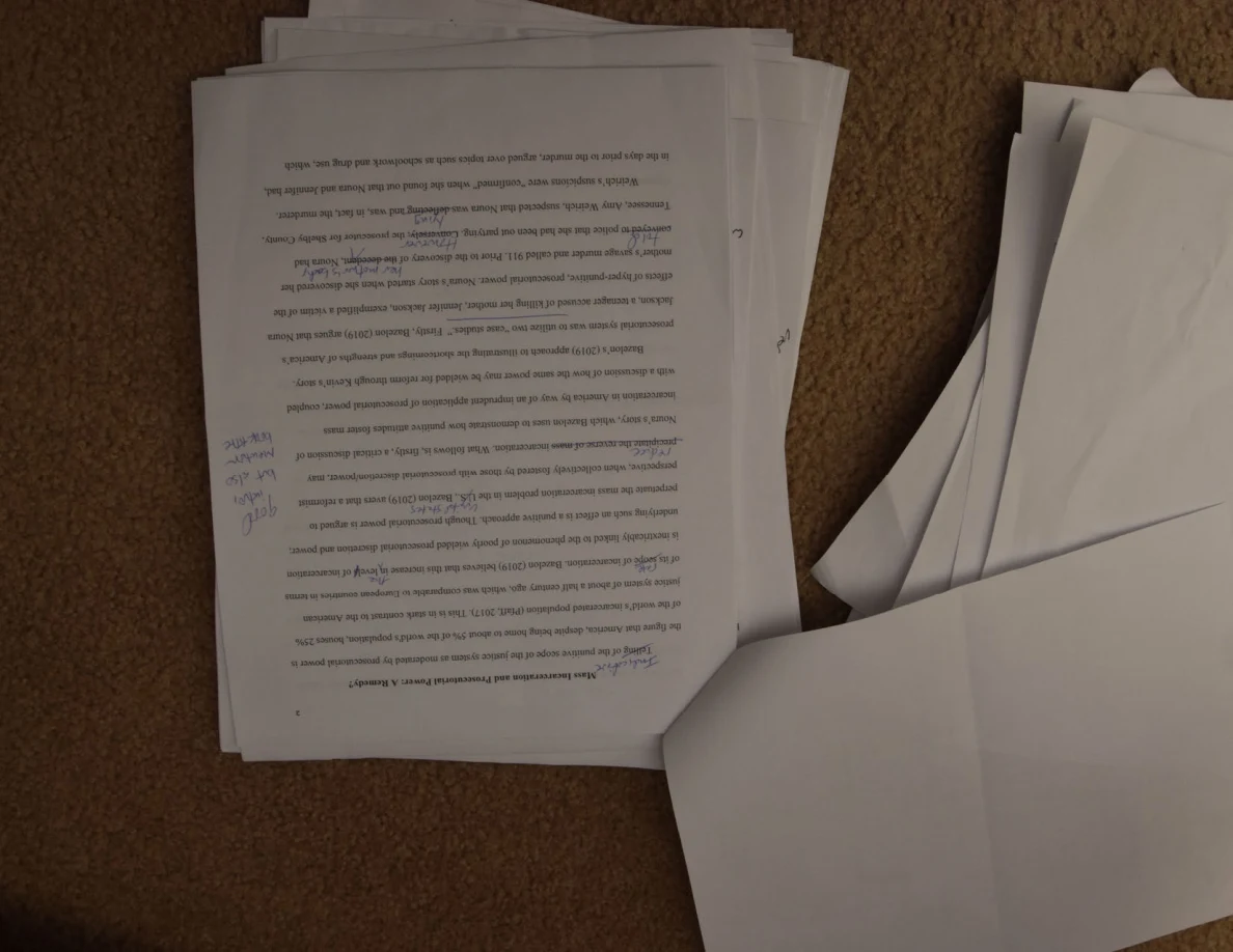 Upside-down printed essay page with blue handwritten comments in the margin.
