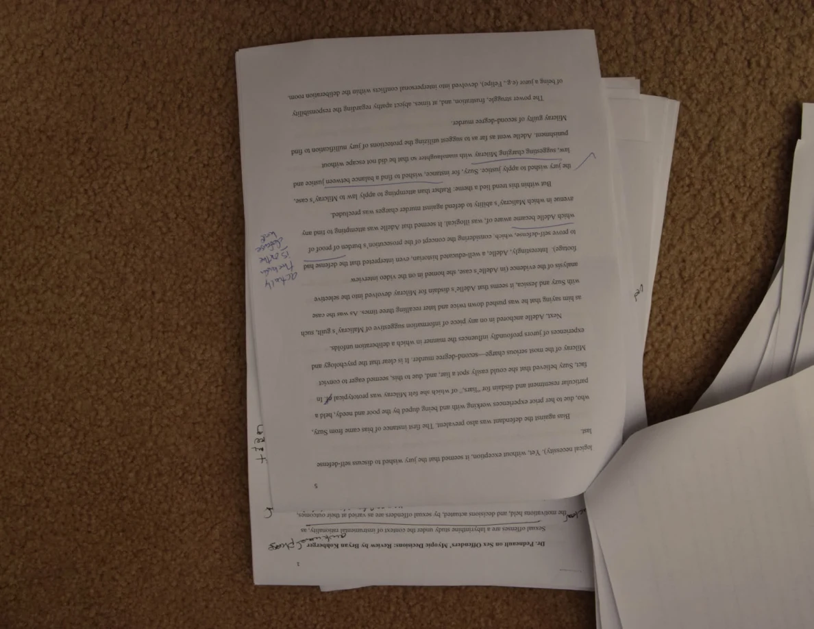 Annotated printed essay page on carpet, oriented upside down beside a turned sheet.