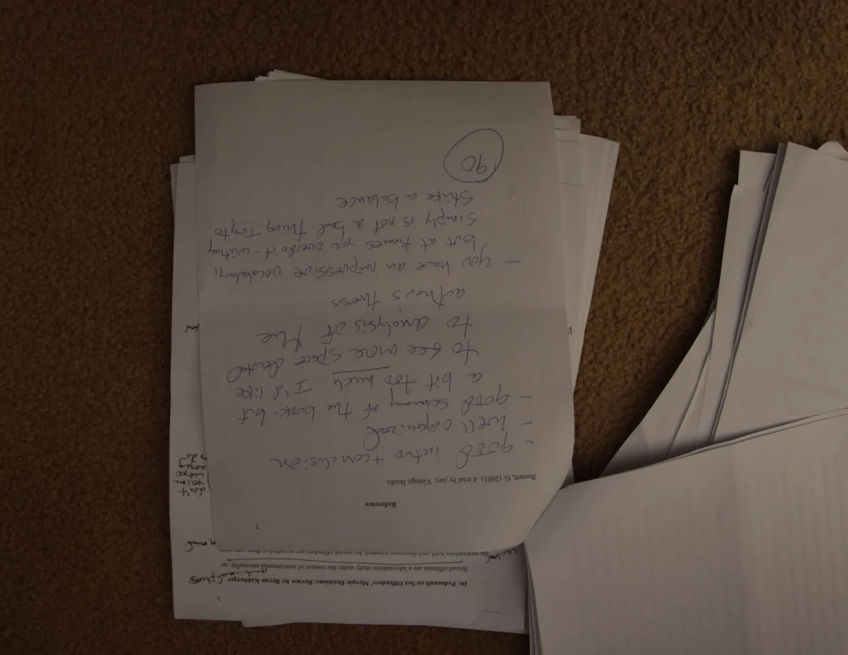 Page with a large handwritten feedback passage and circled number, oriented upside down on a stack.