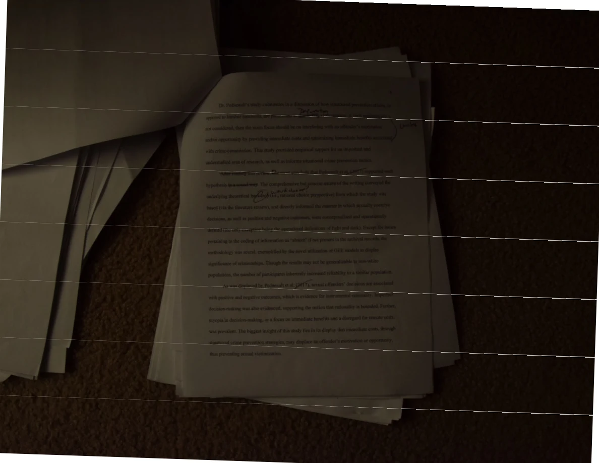 Dim photograph of an annotated printed page on a paper stack, with horizontal image bands.
