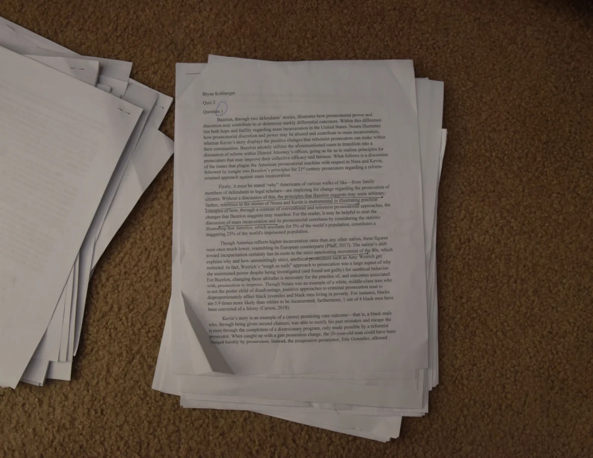 Printed essay page with a circled handwritten mark near the heading, beside another paper stack.