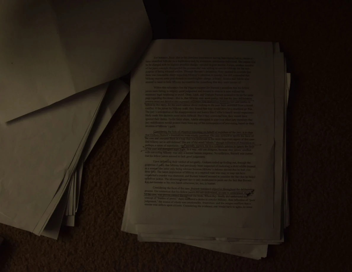 Dim photograph of a printed essay page with a small handwritten correction near its lower right.