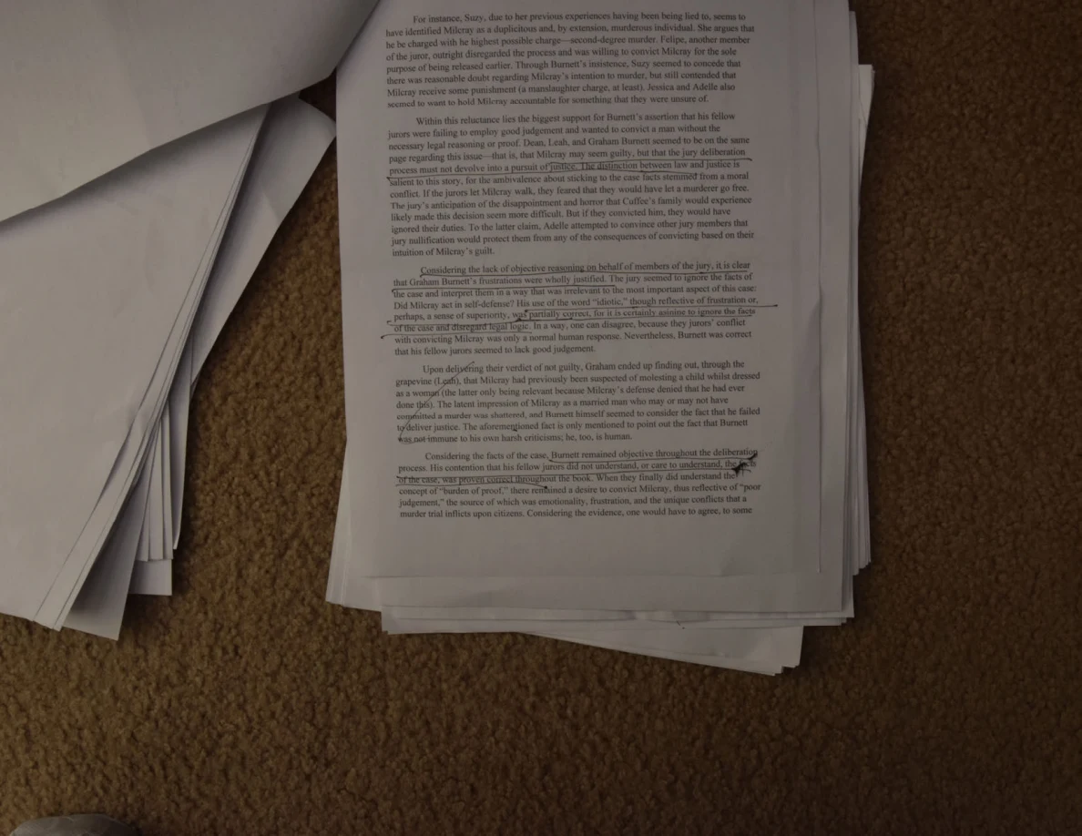 Printed essay page with paragraphs and small handwritten annotations, beside a turned sheet.