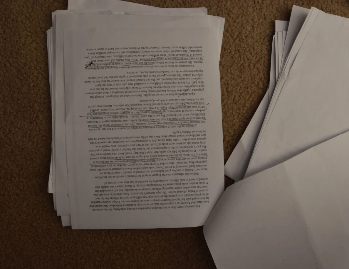 Upside-down printed essay page with handwritten corrections, on a paper stack.