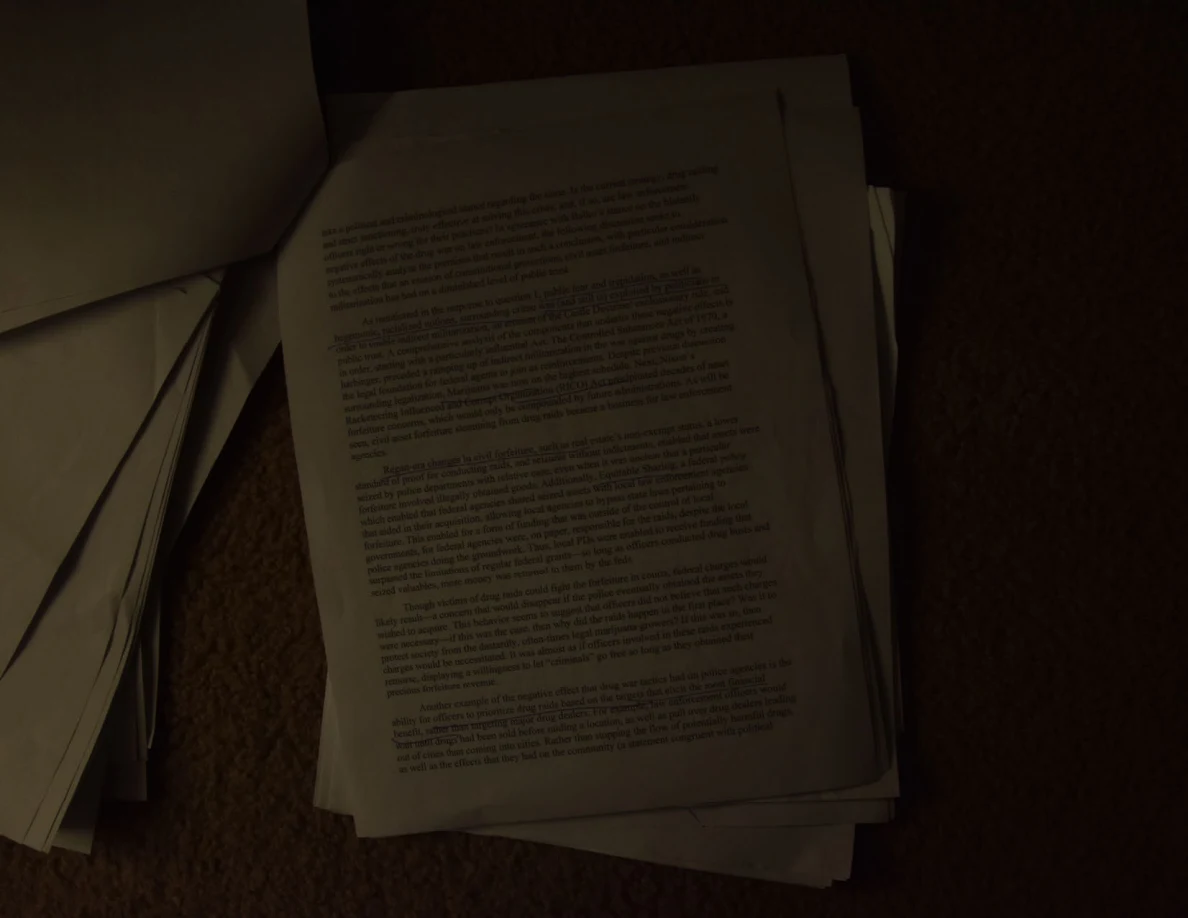 Dim photograph of a printed essay page on a paper stack on carpet.