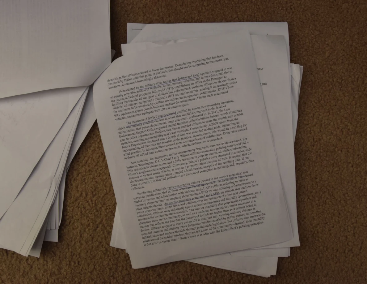 Printed essay page angled across a stack of loose papers on carpet.