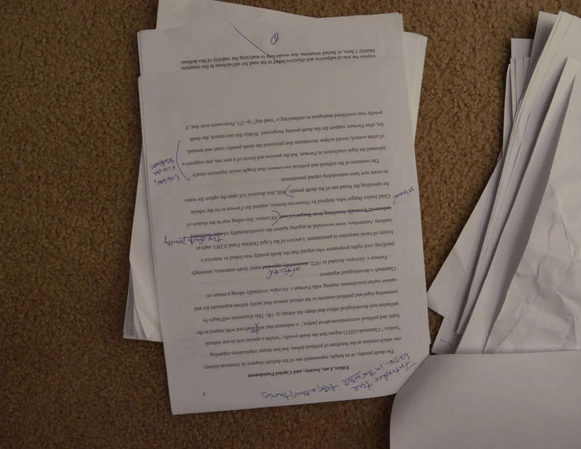 Upside-down printed essay page with handwritten corrections across several paragraphs.