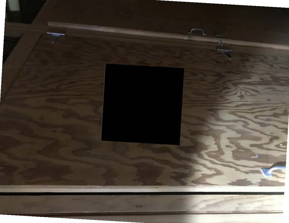 Plywood panel with metal handles and latches, with a large black redaction covering its center.