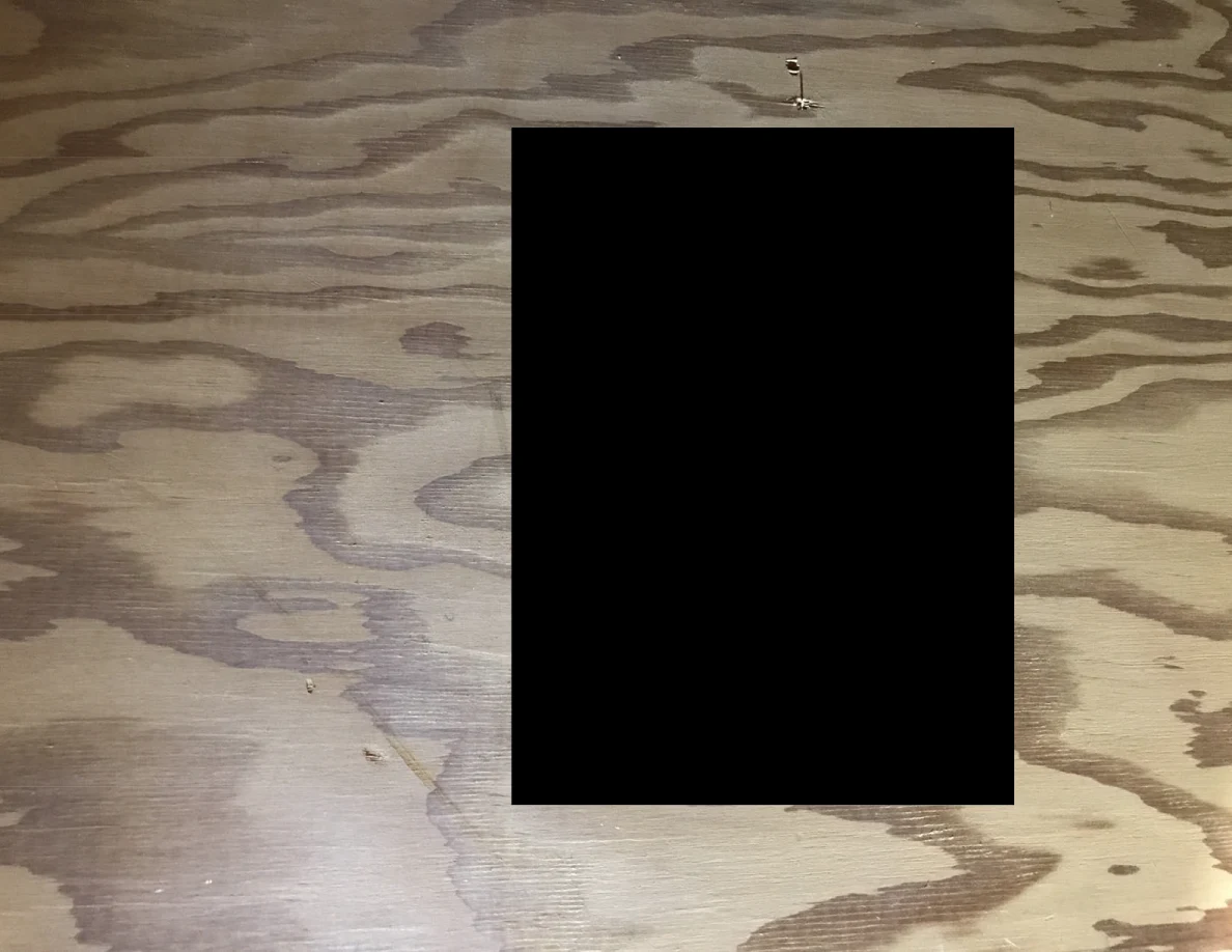 Close view of wood grain on a plywood panel, with a large black rectangular redaction.