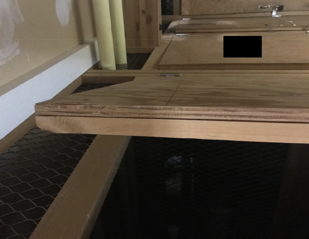 Angled view along wooden storage panels with handles and wire mesh below; one panel has a black redaction.