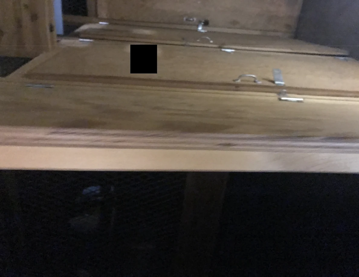 Wooden panel doors with handles and latch hardware above dark wire mesh, with a black redaction.
