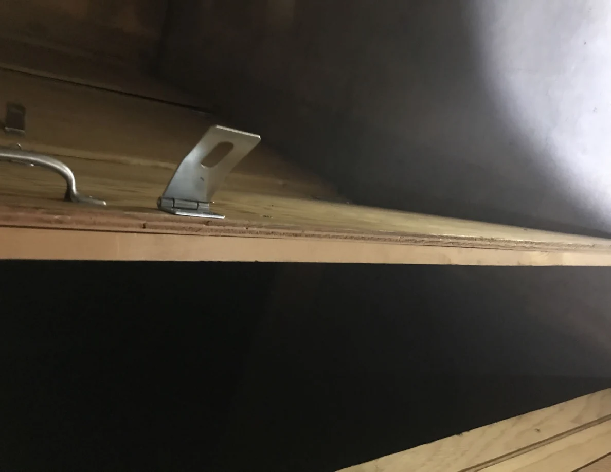 Close view of an upright metal hasp and pull handle on the edge of a plywood panel.