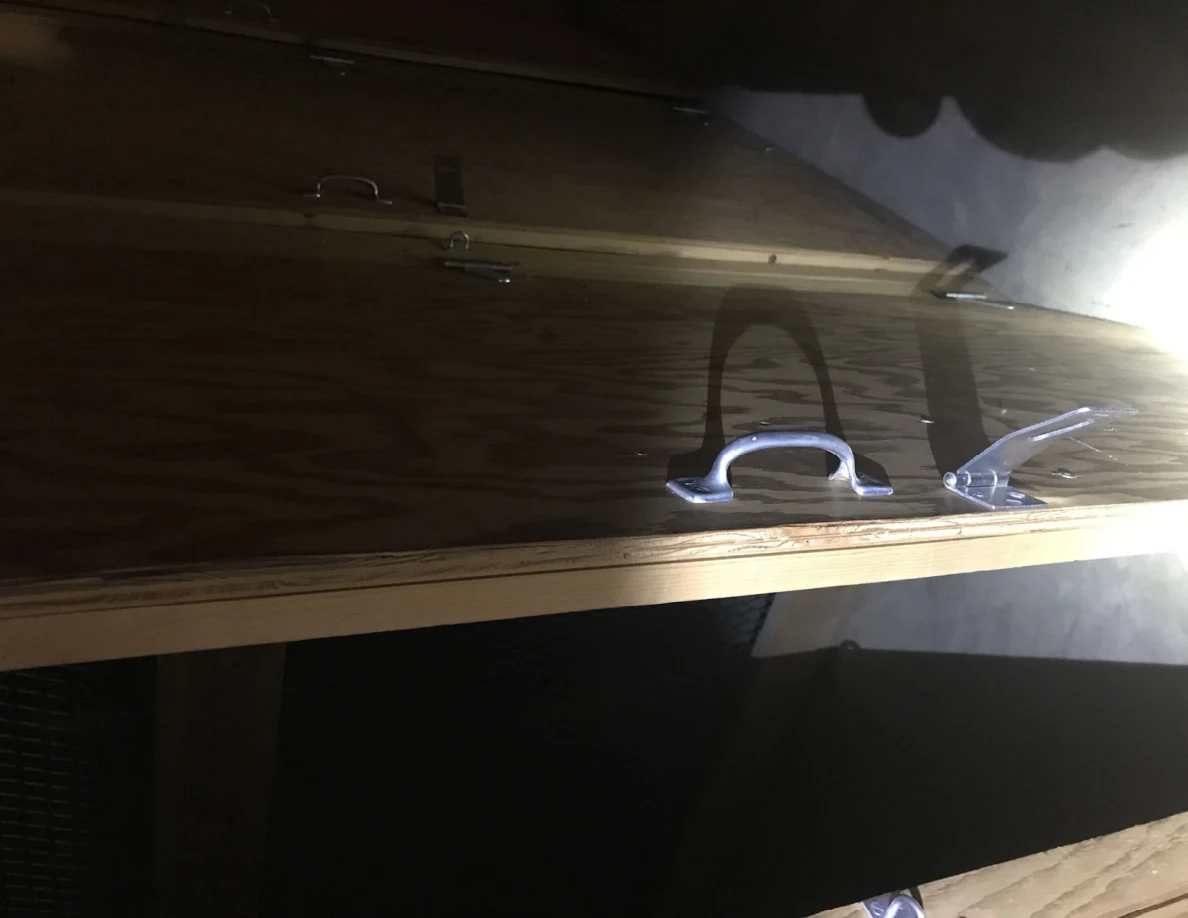 Plywood panels with metal pull handles and latch hardware, lit by a flashlight.