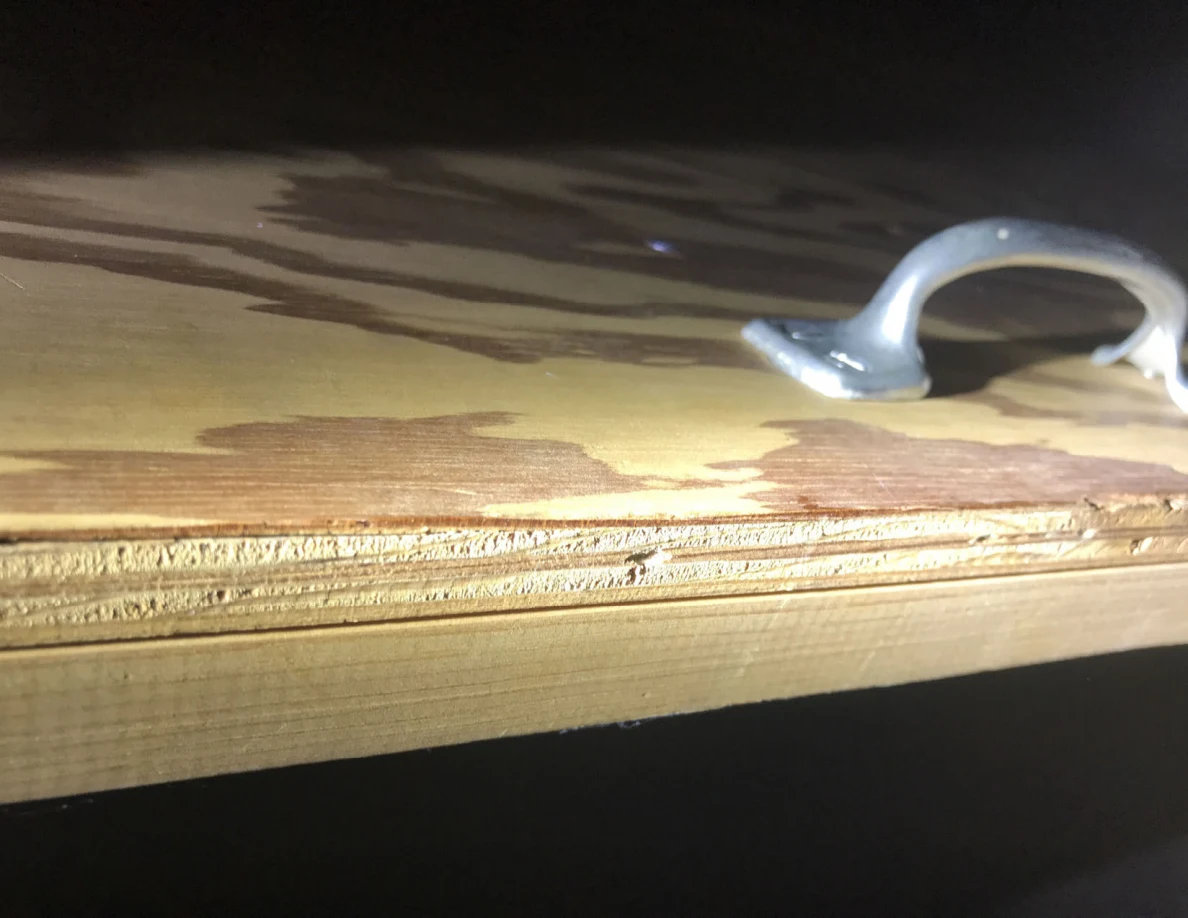Close view of a silver pull handle beside the layered edge of plywood.