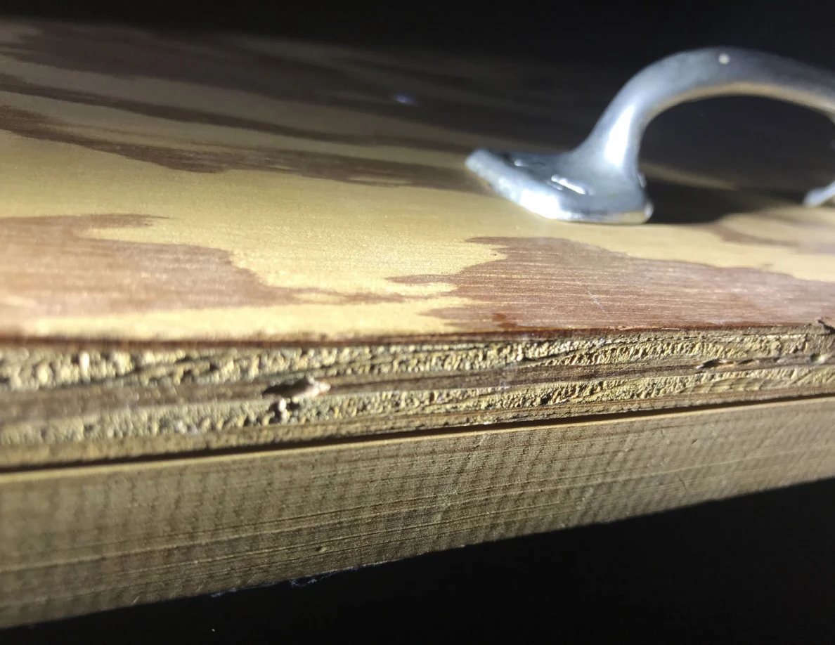 Close view of rough plywood layers below a metal pull handle.