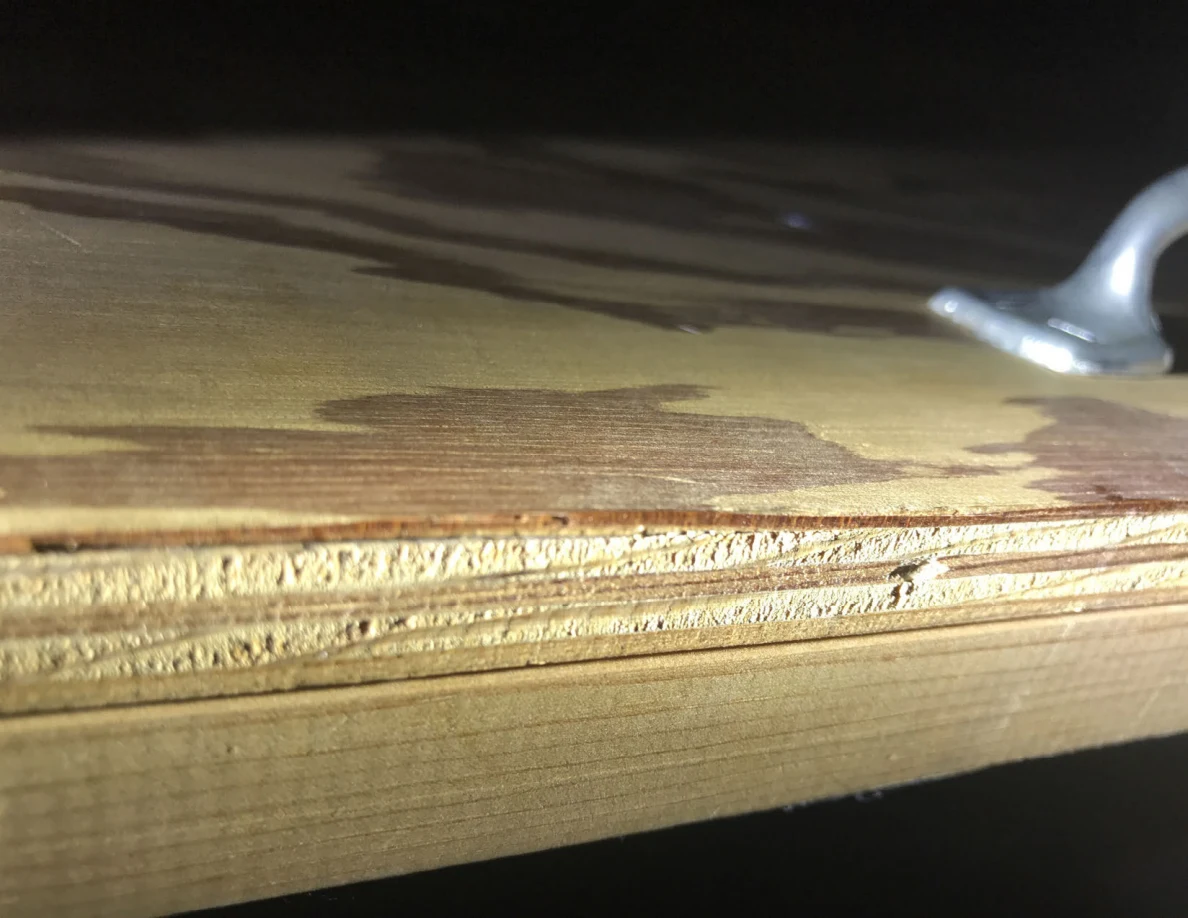 Wood grain and layered edge of a plywood panel with part of a silver handle visible.