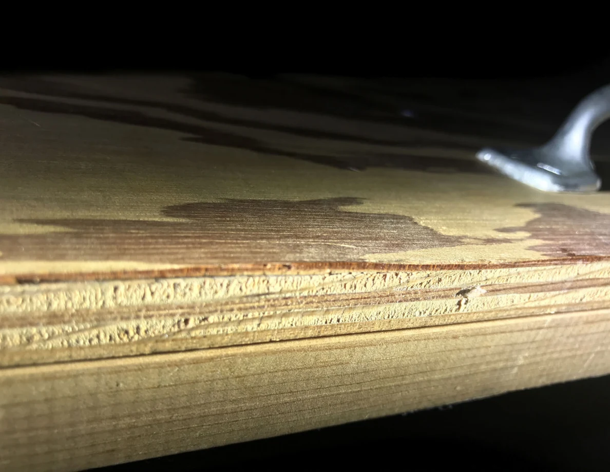 Close view of a worn plywood edge and part of a metal pull handle.
