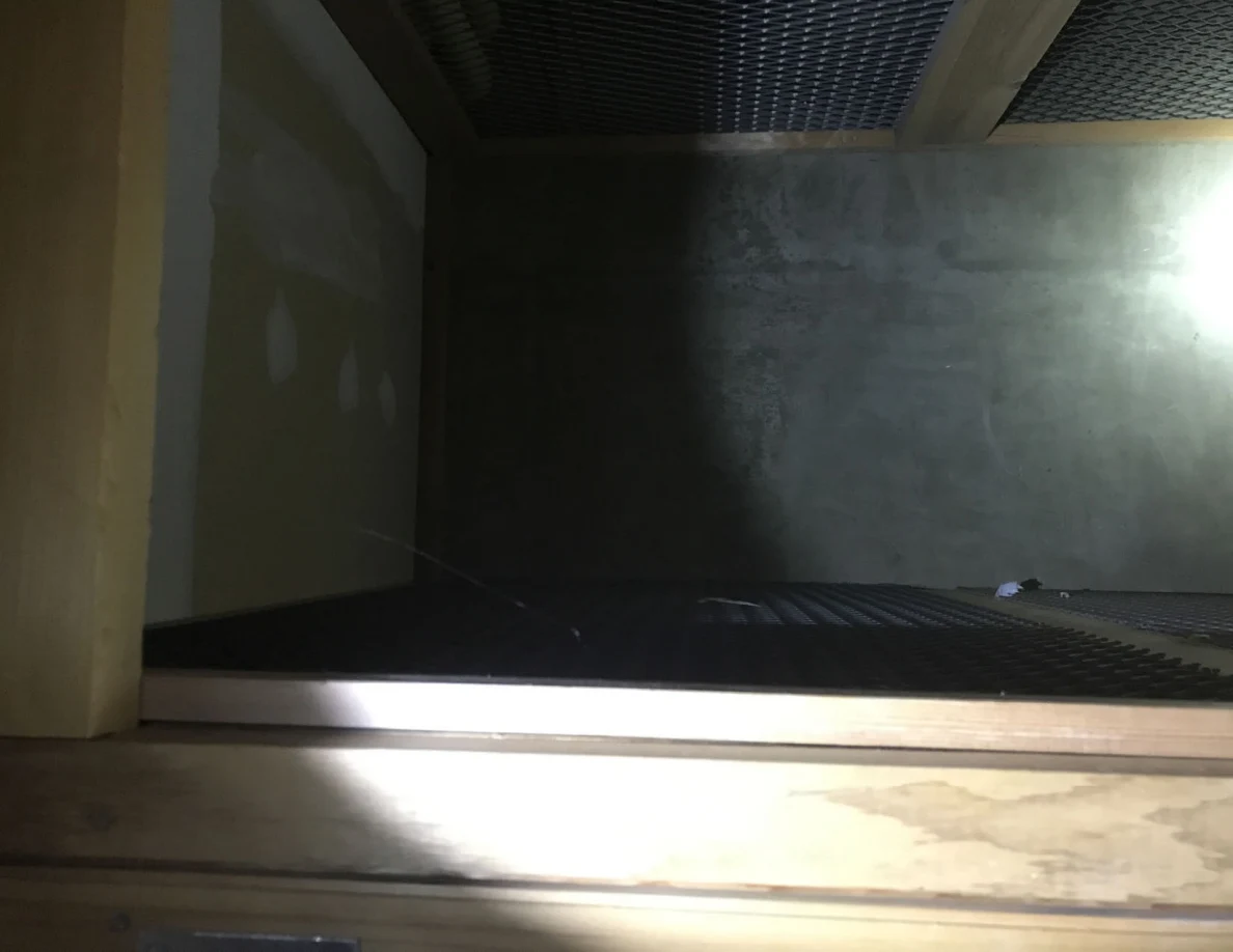 Empty storage compartment with gray walls, wooden framing and wire mesh panels.