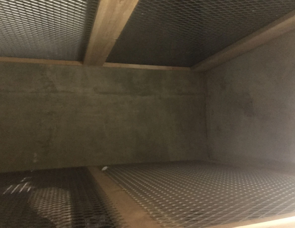 Empty storage compartment with wooden framing and metal mesh floor and ceiling panels.