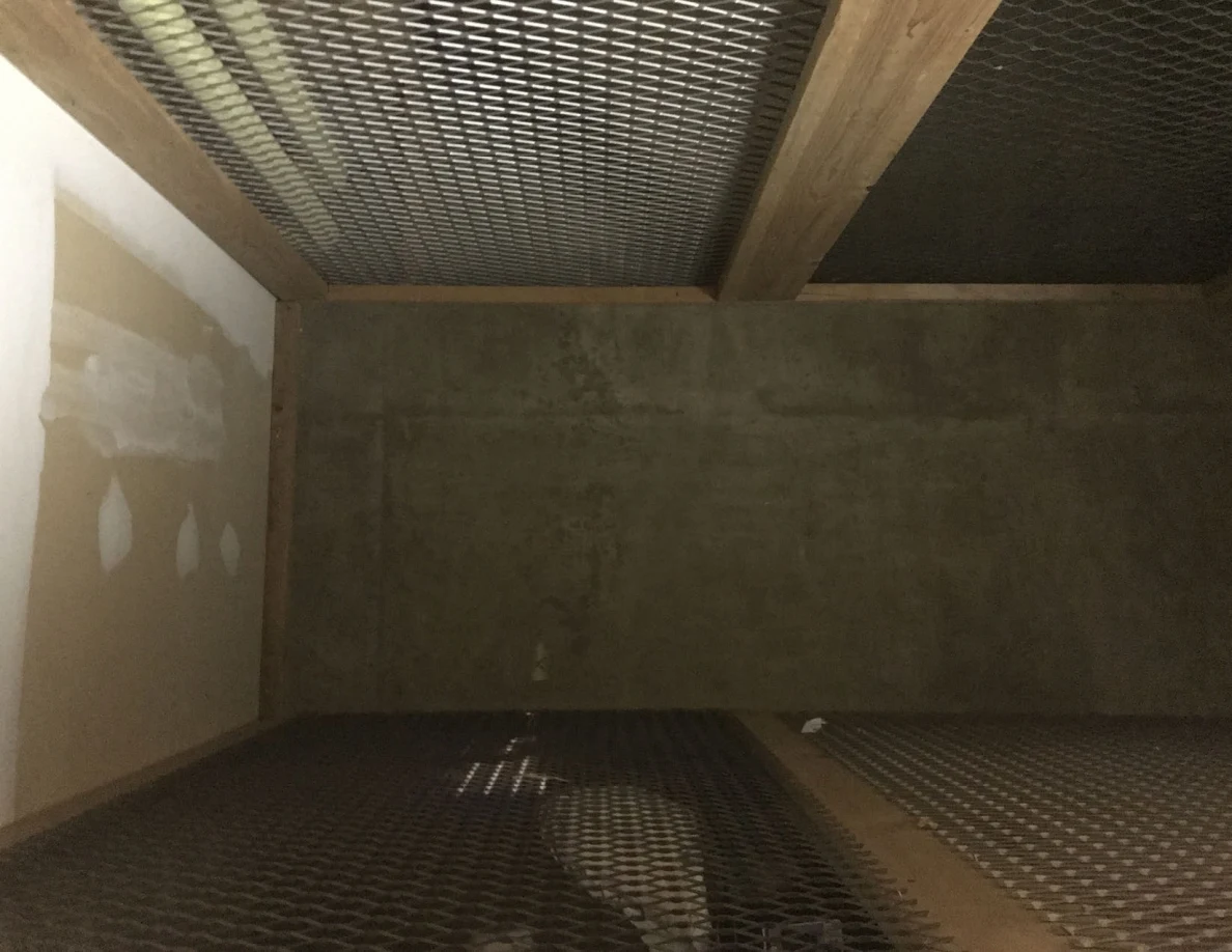 Front view into an empty storage compartment with wire mesh and gray walls.